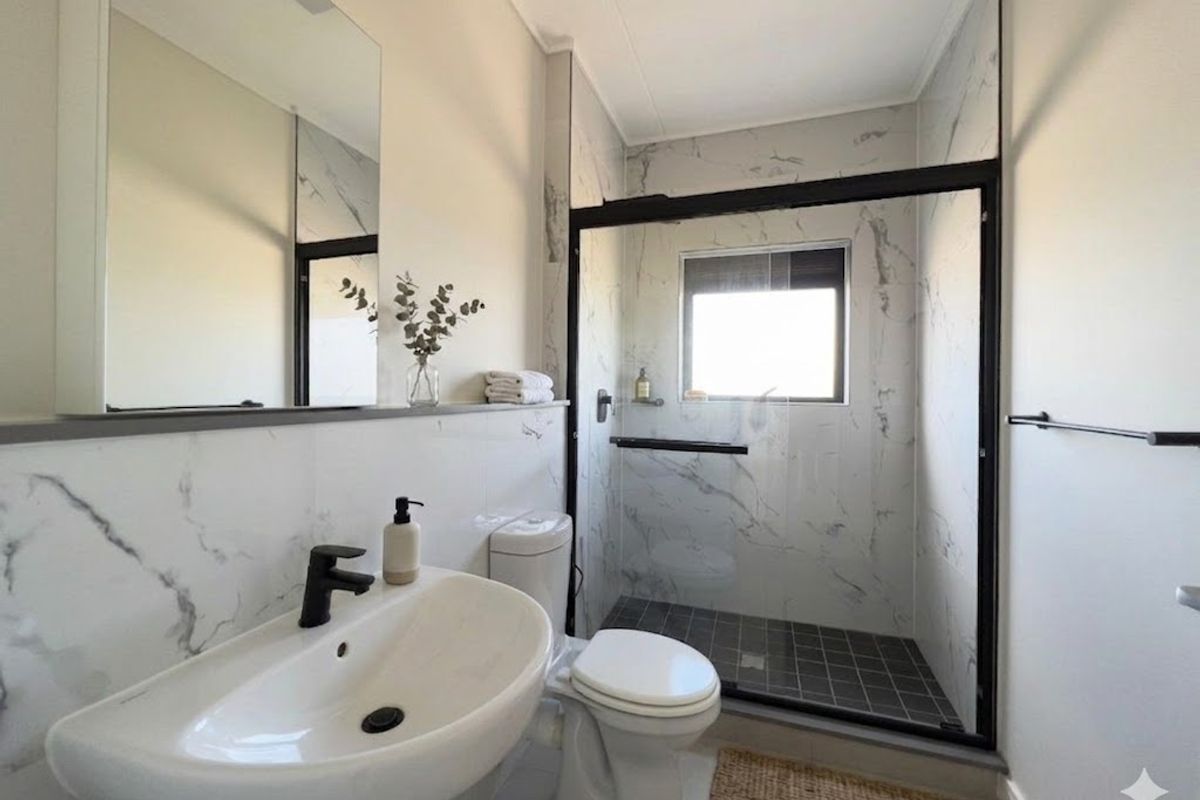 Modern bathroom featuring marble-look wall tiles, a walk-in shower with black frame, pedestal basin, and contemporary black tapware.