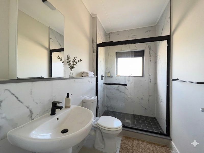 Modern bathroom featuring marble-look wall tiles, a walk-in shower with black frame, pedestal basin, and contemporary black tapware.