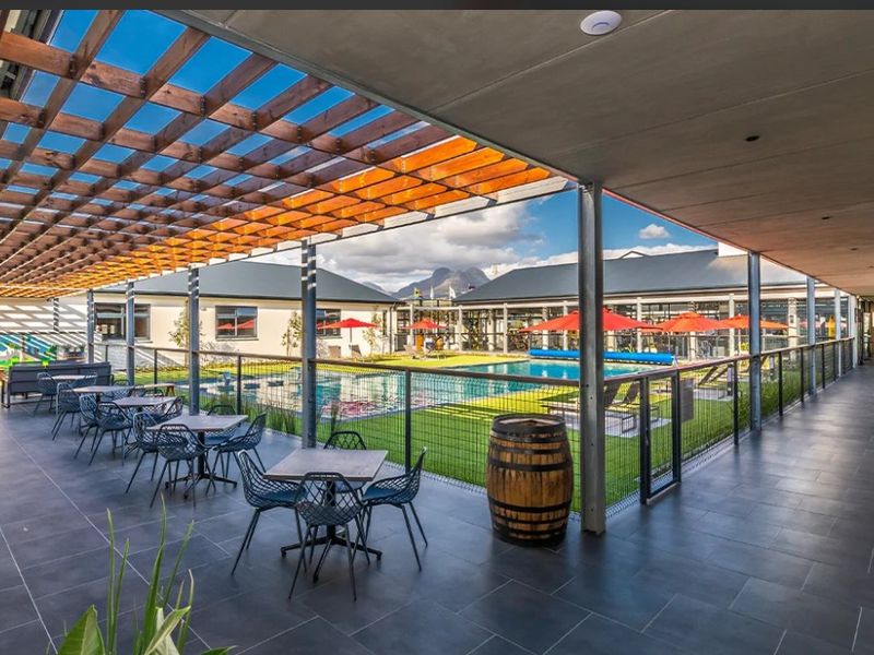Spacious covered patio area featuring a timber pergola, dark tiled flooring, and direct views overlooking the communal swimming pool and landscaped grounds.
