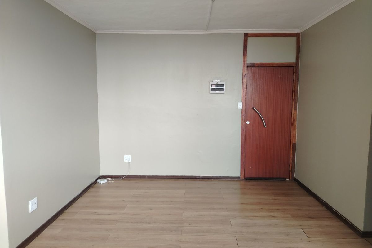 An empty living room featuring laminate flooring, a timber entrance door, and neutral wall tones, providing a blank canvas for interior design.