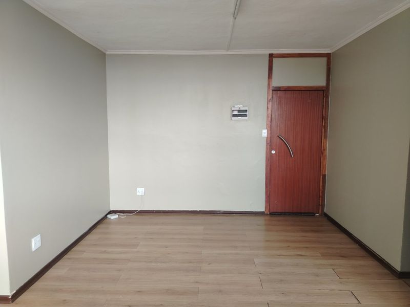 An empty living room featuring laminate flooring, a timber entrance door, and neutral wall tones, providing a blank canvas for interior design.