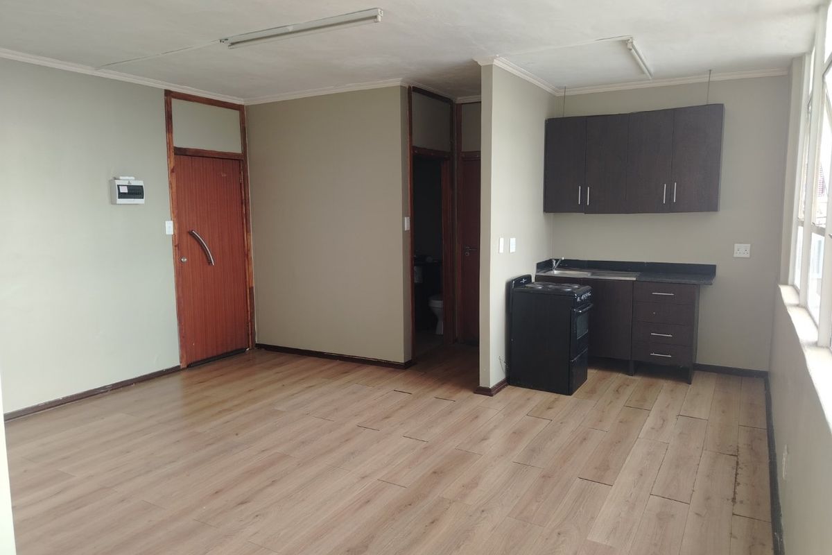 Open-plan living area featuring laminate flooring, a compact kitchen with built-in cabinetry, and a freestanding stove.