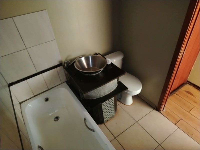 A compact bathroom featuring a bathtub, toilet, and a vessel sink vanity with tiled splashback and flooring.