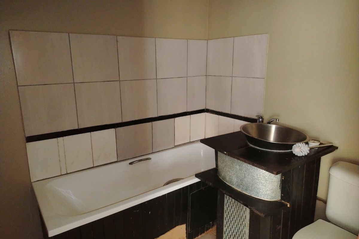 A dated bathroom featuring a bathtub, vessel sink vanity, and toilet with wall tiling. The space requires cosmetic updates and repairs to fixed finishes.