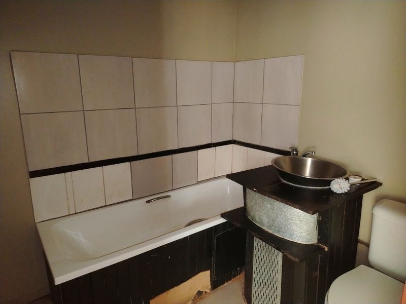 A dated bathroom featuring a bathtub, vessel sink vanity, and toilet with wall tiling. The space requires cosmetic updates and repairs to fixed finishes.