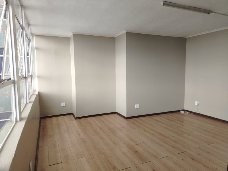 A bright, empty living area featuring modern laminate flooring, neutral wall tones, and large windows that provide ample natural light.