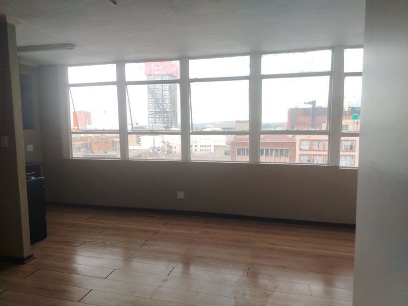 An empty living area featuring large windows with city views and laminate flooring, offering a blank canvas for interior design.