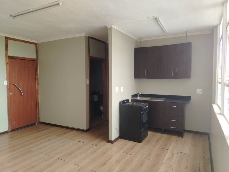 Open plan living area featuring laminate flooring and a compact kitchenette with built-in cabinetry and a freestanding stove.