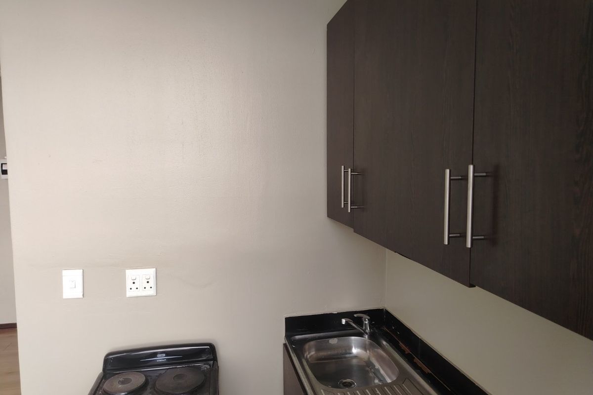 A compact kitchen area featuring dark wood cabinetry, a stainless steel sink with a mixer tap, black granite countertops, and a freestanding stove.