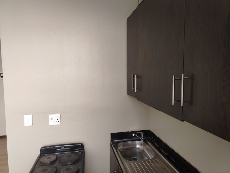 A compact kitchen area featuring dark wood cabinetry, a stainless steel sink with a mixer tap, black granite countertops, and a freestanding stove.