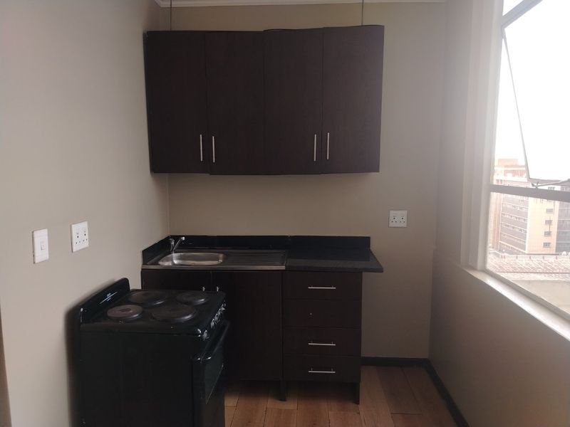 Compact kitchen area featuring dark cabinetry, stone countertops, a stainless steel sink, and a freestanding electric stove.