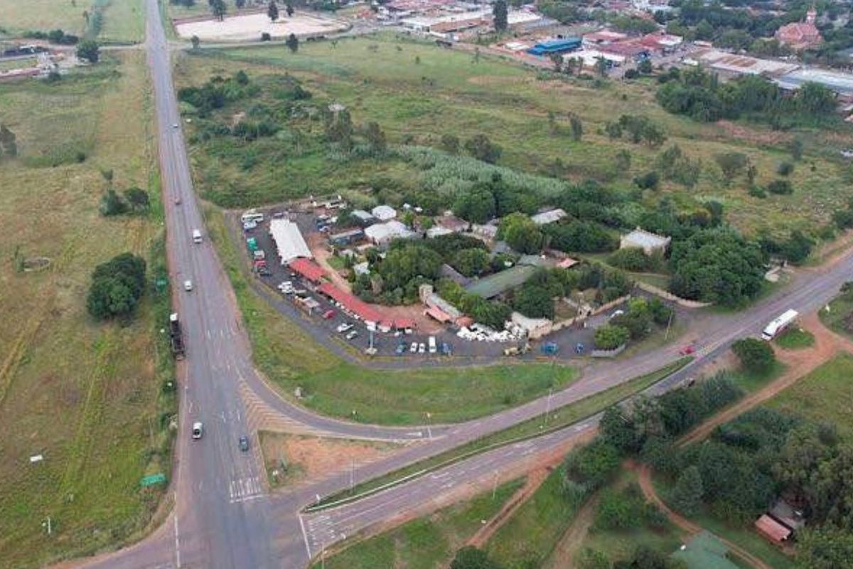 Aerial view of a commercial property complex with road frontage, featuring multiple structures and paved parking areas.