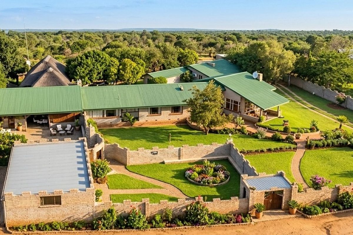 Aerial view of a commercial property featuring multiple buildings with green metal roofs, extensive landscaped gardens, and secure brick boundary walls.