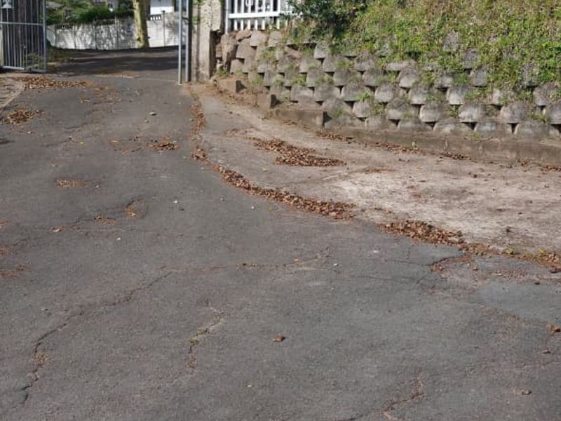 A view of the property entrance featuring a metal gate, a retaining wall, and an asphalt driveway showing signs of wear.