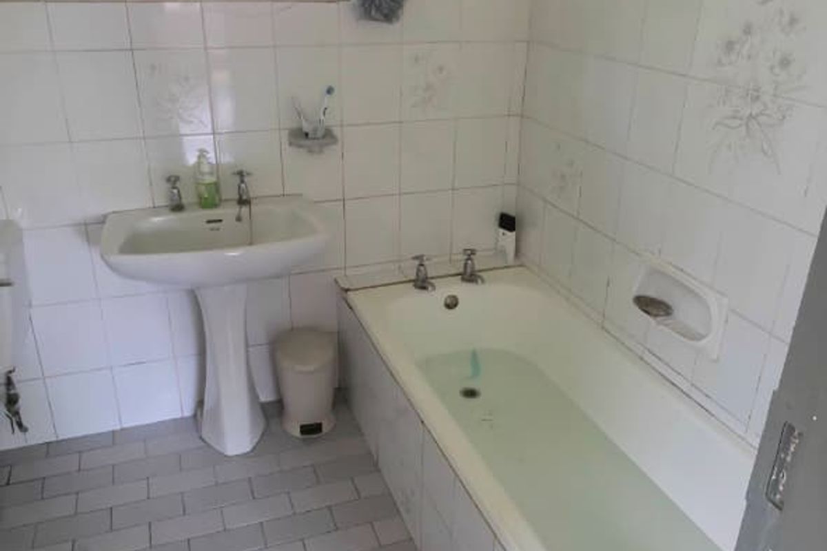A dated bathroom featuring a pedestal basin, built-in bathtub, and full-height wall tiling. The space requires cosmetic updates to modernize the finishes.