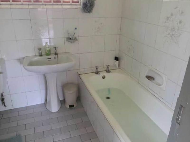 A dated bathroom featuring a pedestal basin, built-in bathtub, and full-height wall tiling. The space requires cosmetic updates to modernize the finishes.