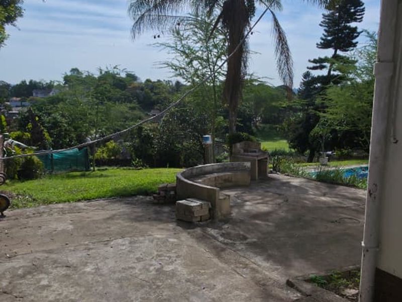 Outdoor patio area featuring a built-in masonry bench and braai, overlooking a garden with mature trees.