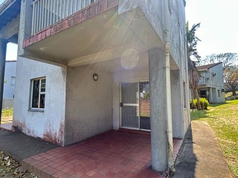 Rear view of the townhouse featuring a covered patio area, a balcony above, and access via a sliding glass door.