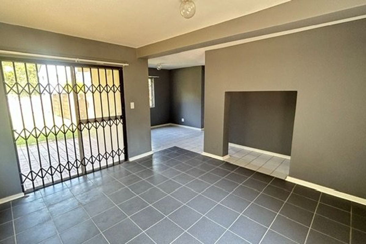 An empty living area featuring dark tiled flooring, a sliding glass door with a security gate, and a recessed wall niche.