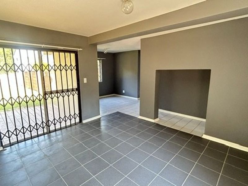 An empty living area featuring dark tiled flooring, a sliding glass door with a security gate, and a recessed wall niche.