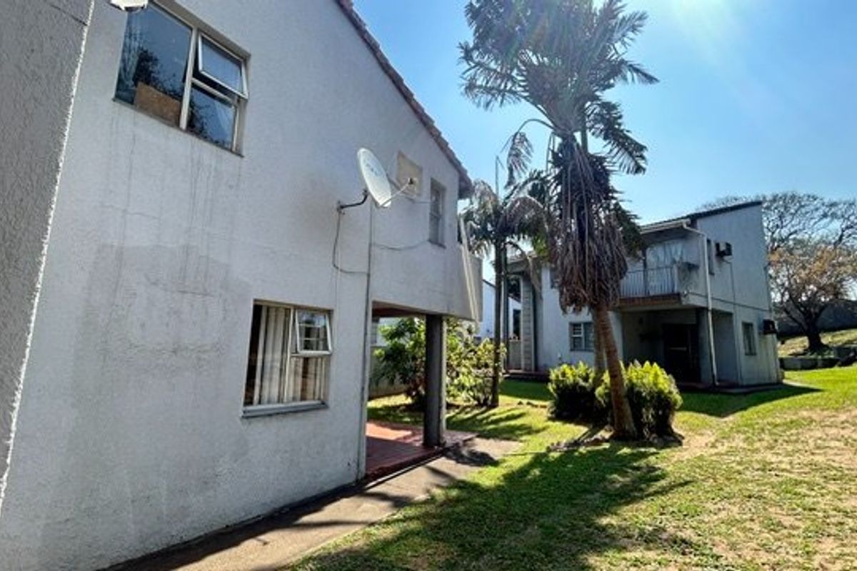 Rear view of the townhouse complex showing exterior walls, paved pathways, and shared garden space with mature palm trees.