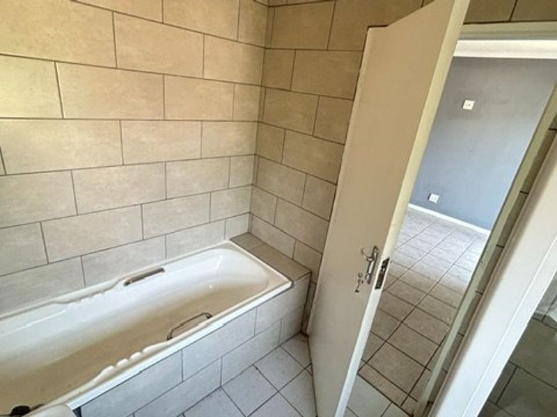 A functional bathroom featuring a built-in bathtub with tiled surround and flooring, offering a neutral base for potential cosmetic updates.
