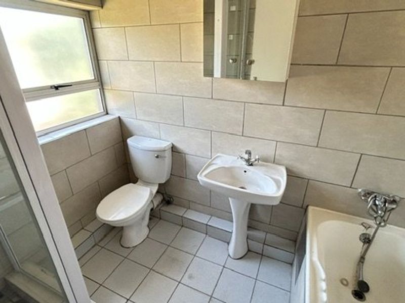 A functional bathroom featuring a pedestal basin, toilet, shower enclosure, and bathtub with neutral wall and floor tiling.