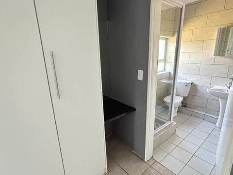 A functional bathroom featuring a pedestal basin, toilet, and shower enclosure, complemented by tiled walls and flooring, with adjacent built-in storage.