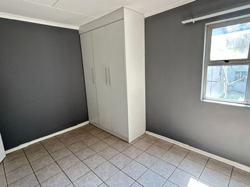A clean, empty bedroom featuring dark grey walls, tiled flooring, and a built-in wardrobe with white cabinetry.