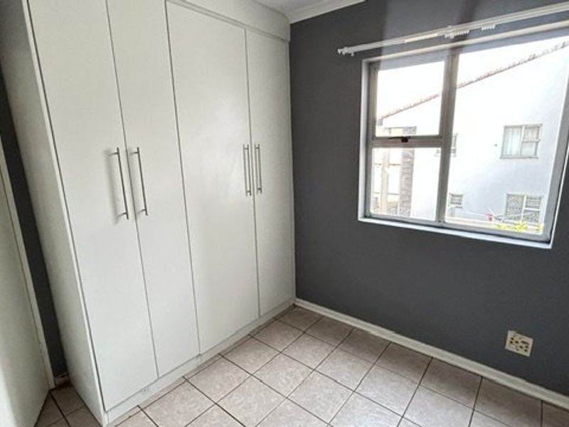 A clean, empty bedroom featuring built-in cupboards, tiled flooring, and a window with an exterior view.