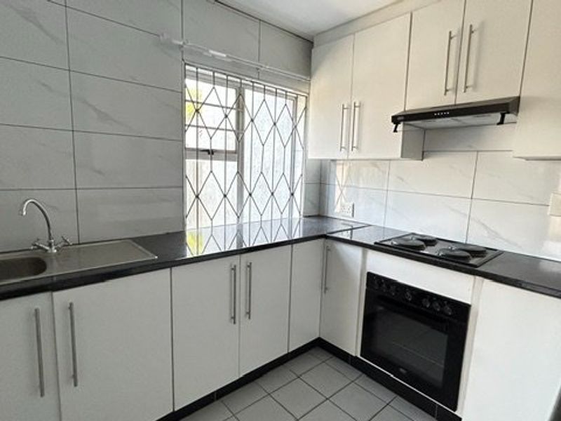 Modern kitchen featuring white cabinetry, dark granite countertops, built-in oven, electric hob, and tiled splashbacks with security bars on the window.