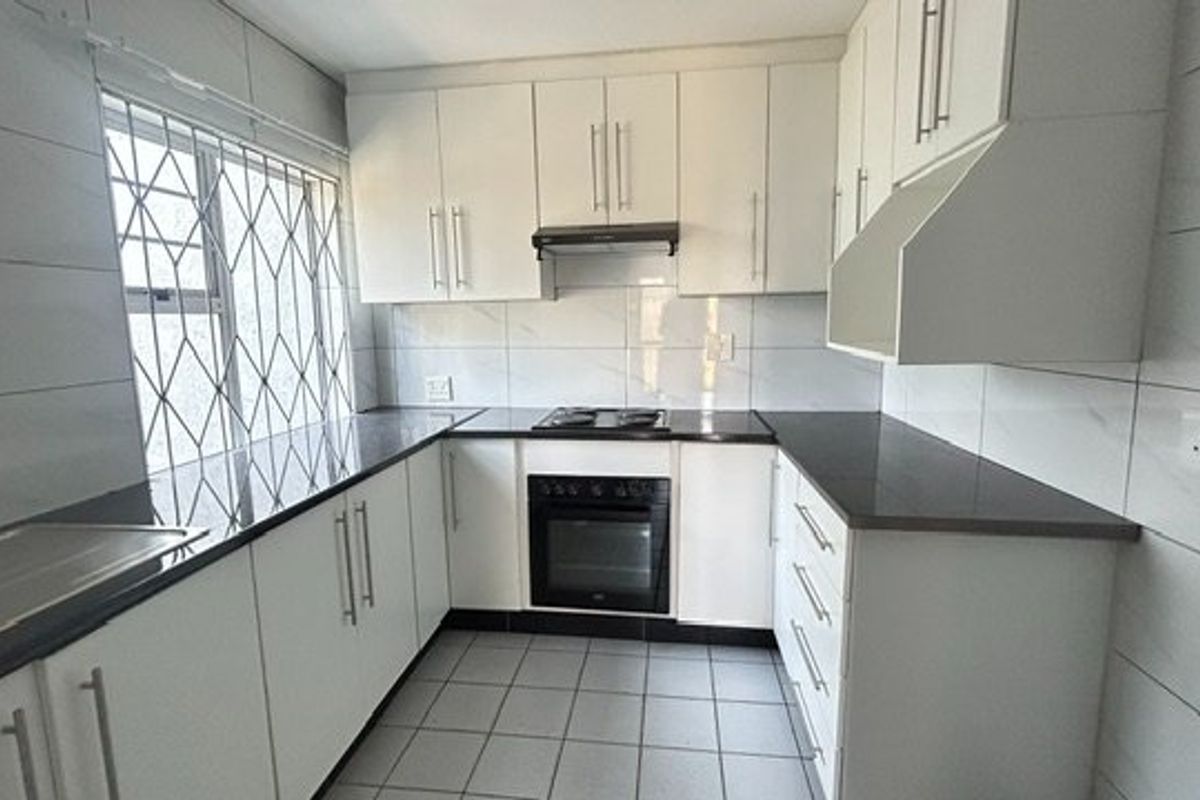 A clean, functional kitchen featuring white cabinetry, dark stone countertops, built-in oven, hob, extractor fan, and tiled finishes throughout.