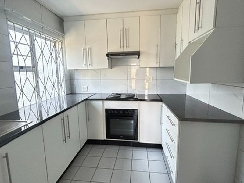A clean, functional kitchen featuring white cabinetry, dark stone countertops, built-in oven, hob, extractor fan, and tiled finishes throughout.