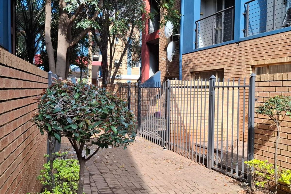 A paved exterior walkway between brick boundary walls and the apartment building, featuring metal security fencing and access to the lower level.