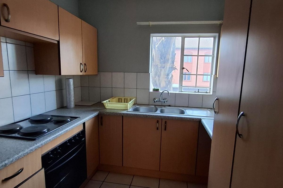 A functional kitchen featuring laminate cabinetry, a built-in oven with electric hob, and a double bowl sink with tiled backsplash.