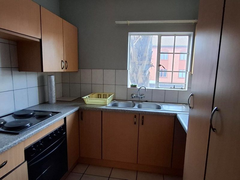 A functional kitchen featuring laminate cabinetry, a built-in oven with electric hob, and a double bowl sink with tiled backsplash.