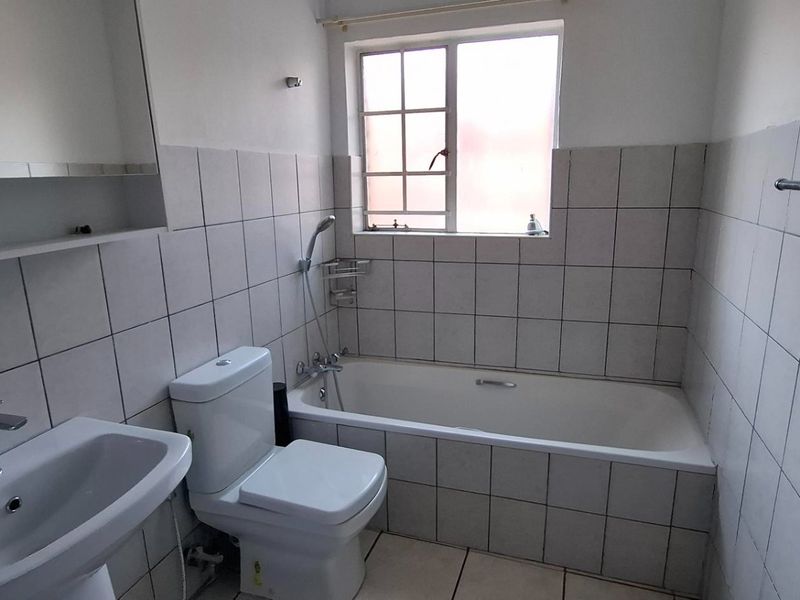 A functional bathroom featuring a pedestal basin, toilet, and bathtub with tiled walls and flooring, offering a clean, neutral canvas for updates.