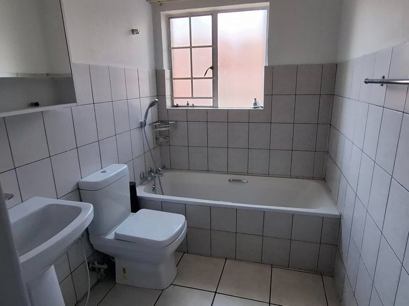 A functional bathroom featuring a pedestal basin, toilet, and bathtub with full-height wall tiling and tiled flooring.