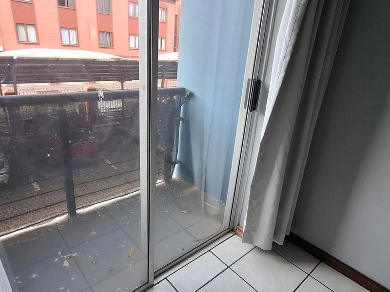 A small balcony accessed via a sliding glass door, featuring tiled flooring and a metal railing overlooking a parking area.