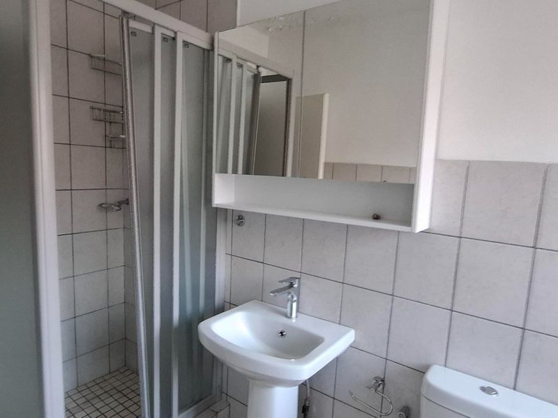 A functional bathroom featuring a pedestal sink, a shower enclosure with a glass door, and a wall-mounted mirrored medicine cabinet with tiled walls.