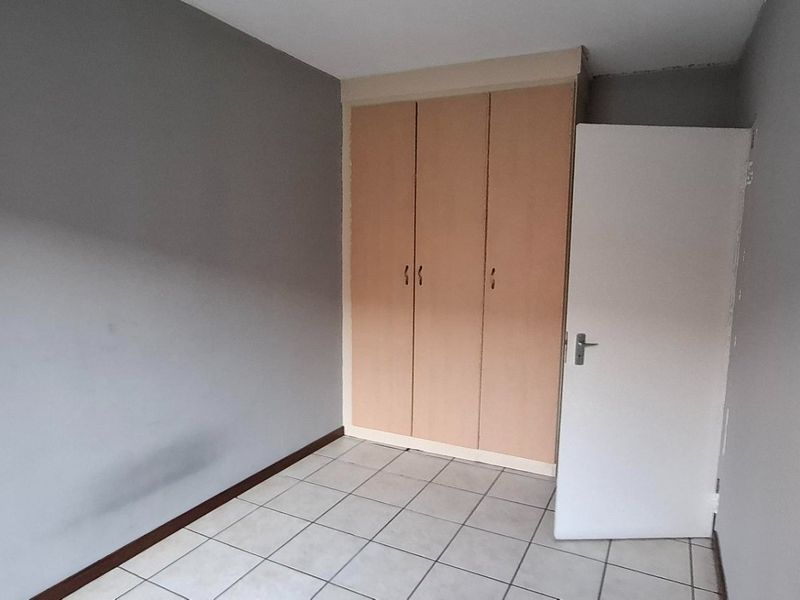 An empty bedroom featuring tiled flooring and built-in wooden cupboards, requiring minor cosmetic updates to the wall finishes.