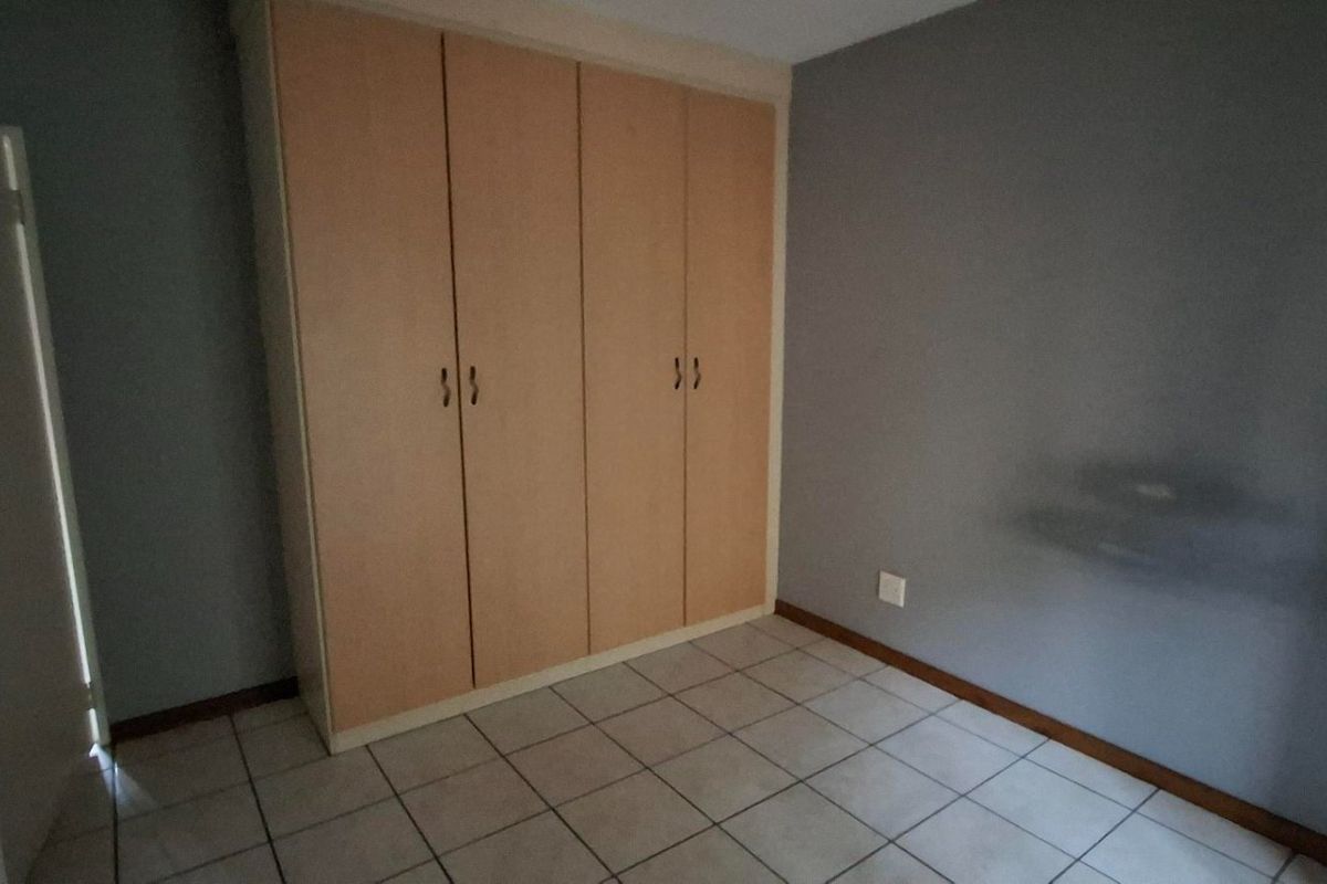A vacant bedroom featuring neutral grey walls, light-toned built-in cupboards, and tiled flooring, offering a clean and functional space.