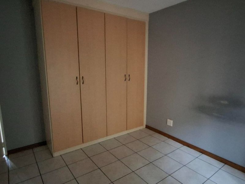 A vacant bedroom featuring neutral grey walls, light-toned built-in cupboards, and tiled flooring, offering a clean and functional space.