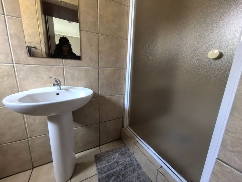 A functional bathroom featuring a pedestal basin, mixer tap, and a shower enclosure with tiled walls and flooring.