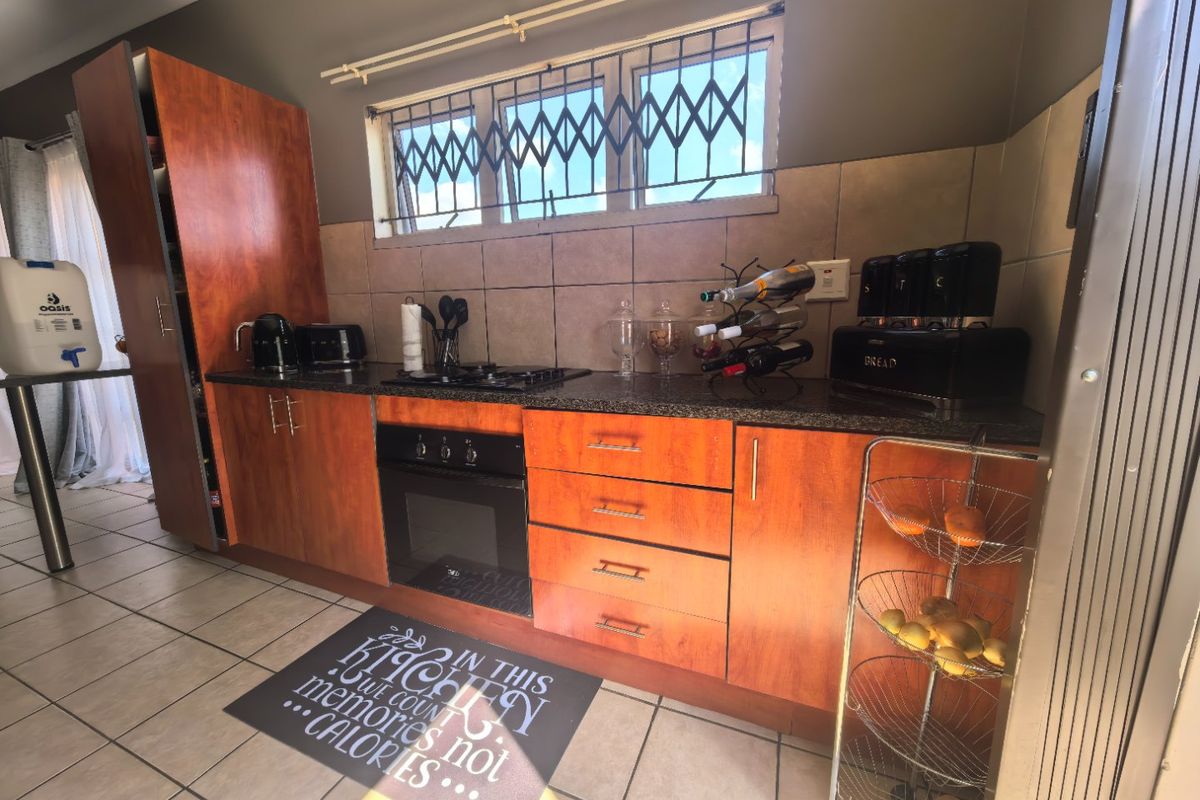 A functional kitchen featuring wood-finish cabinetry, granite countertops, a built-in oven with gas hob, and tiled flooring.
