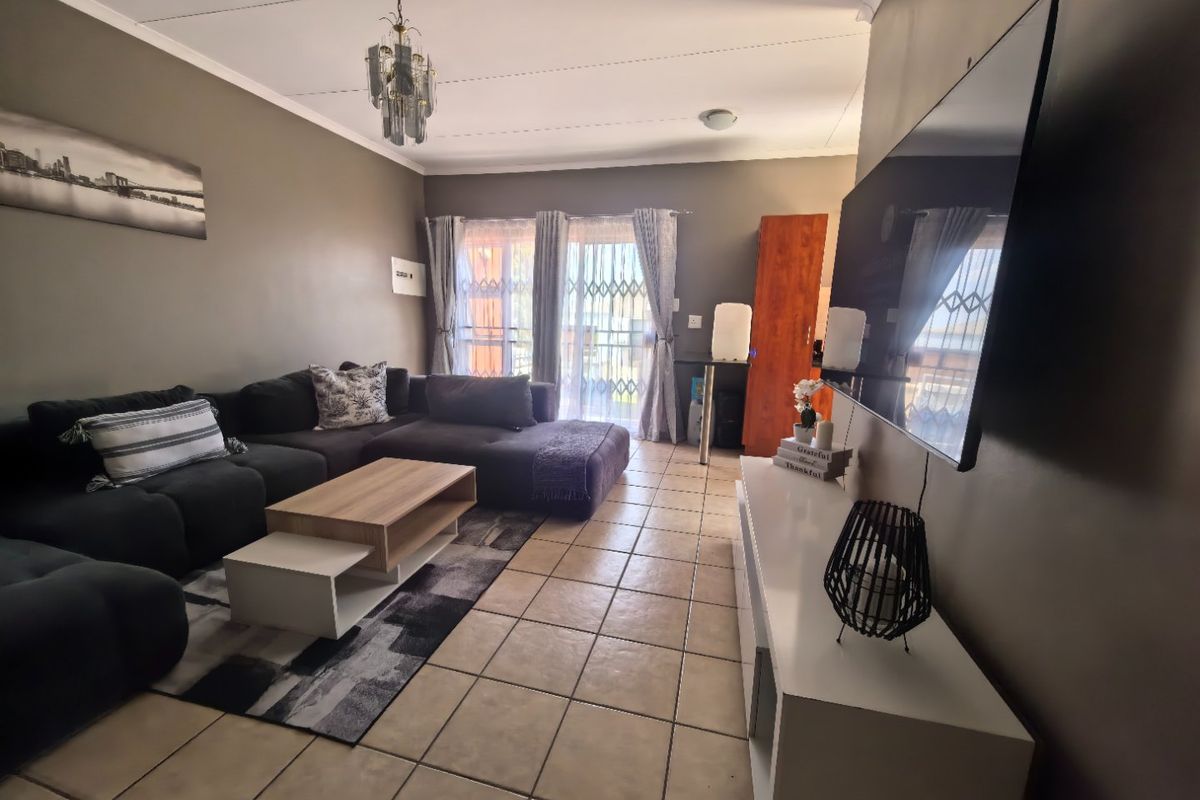 A living room featuring tiled flooring, a ceiling light fixture, and a sliding glass door with a security gate leading to the exterior.
