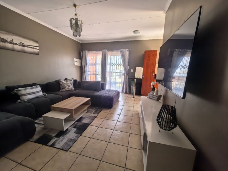 A living room featuring tiled flooring, a ceiling light fixture, and a sliding glass door with a security gate leading to the exterior.