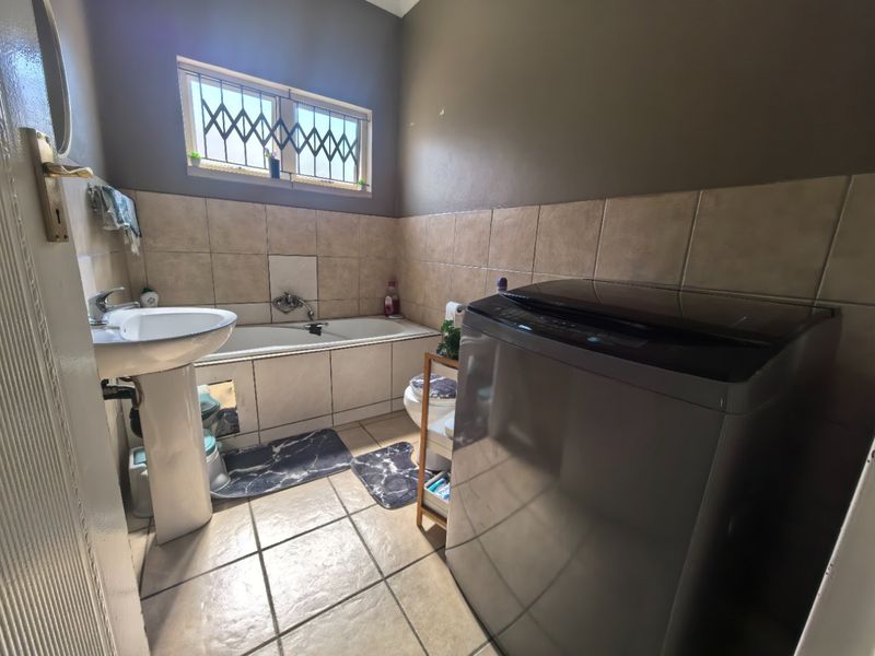 A functional bathroom featuring a pedestal basin, built-in bathtub, and tiled finishes, with a window providing natural light and security bars.
