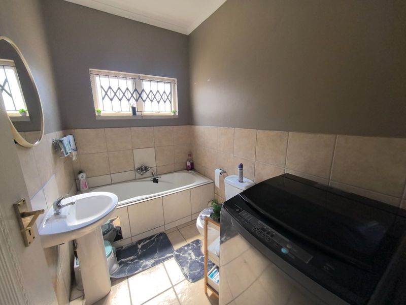 A functional bathroom featuring a pedestal basin, built-in bathtub, and tiled wall finishes, with a window providing natural light.