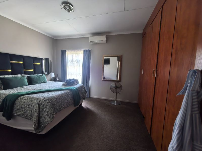 A spacious bedroom featuring built-in wooden cupboards, carpeted flooring, and a wall-mounted air conditioning unit.